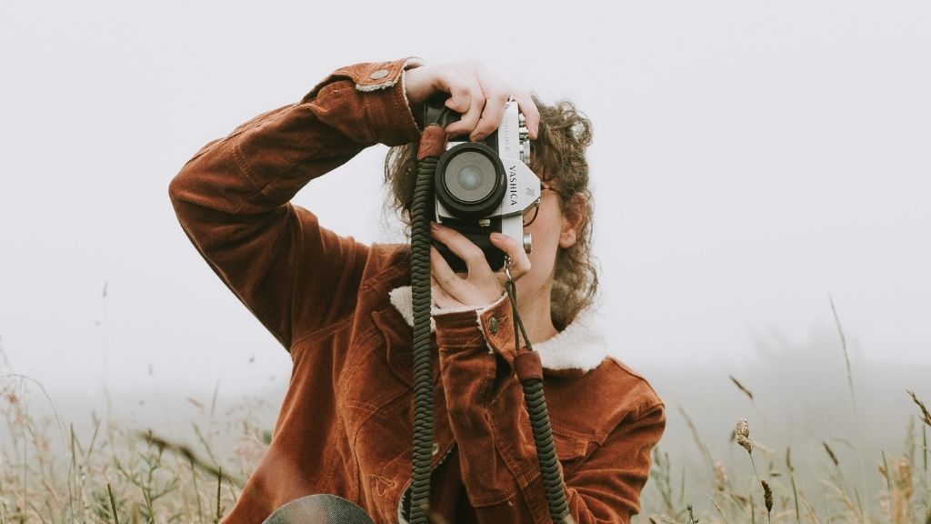 Femme prise de face en train de prendre une photo avec appareil photo vintage