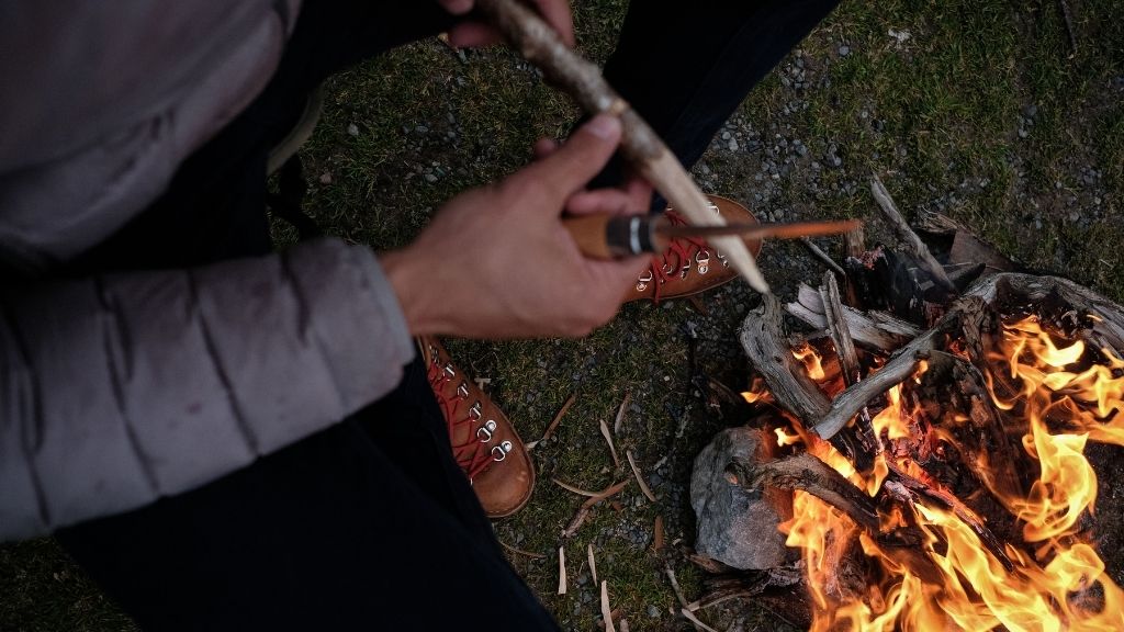 mains d'homme taillant une branche au coin du feu de camp