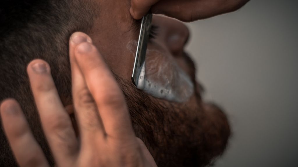 Homme chez le barbier qui se fait faire les contours d'une barbe longue à la shavette, à l'ancienne