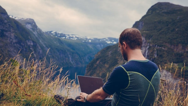 Homme de dos travaillant sur son ordinateur face à la nature, a la montagne. Digital Nomad à la montagne