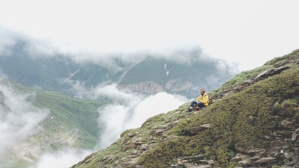 Homme trek assis sur le versant d'une montagne qui scrute le paysage